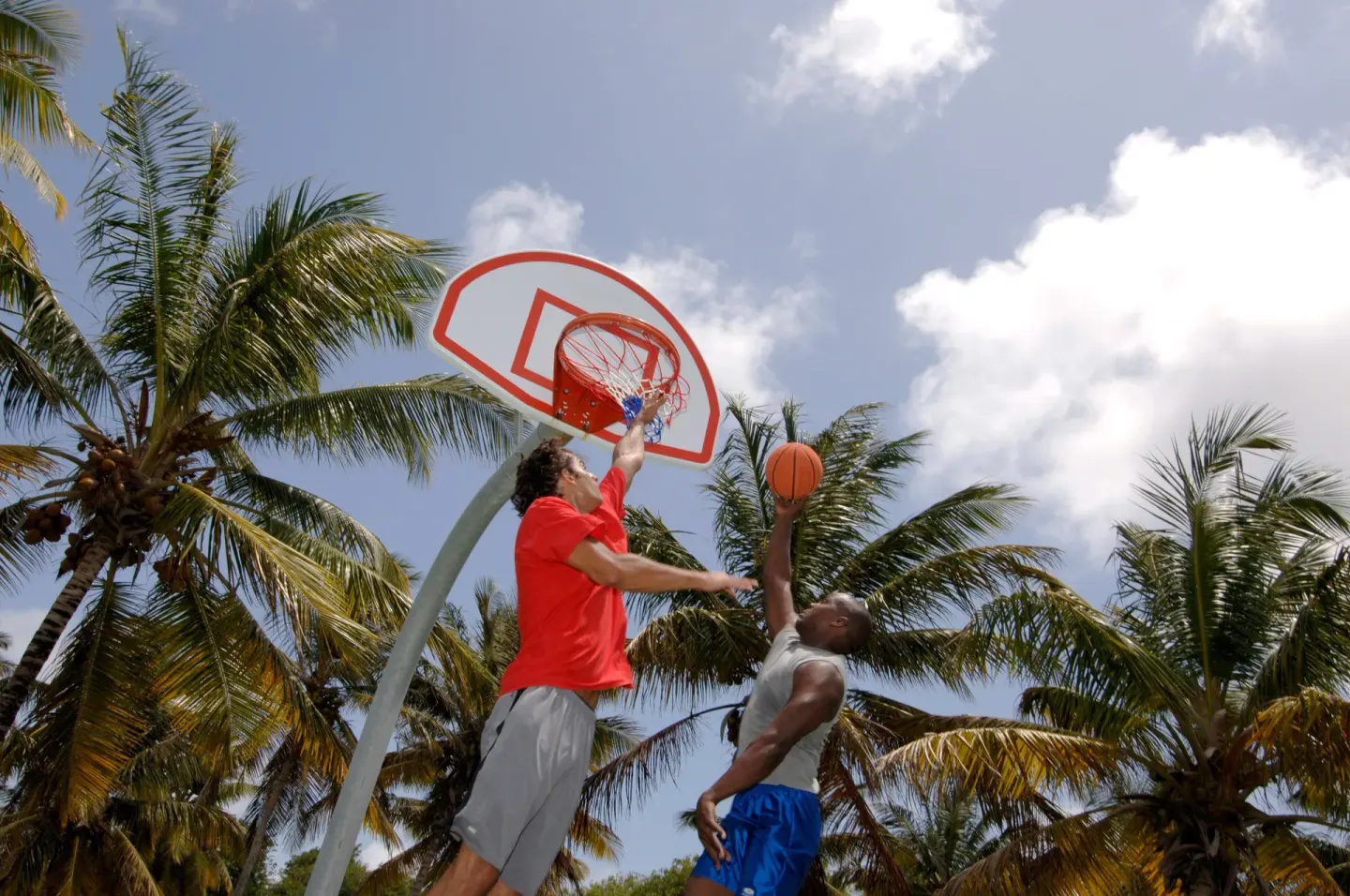 Two guests play basketball under palm trees at Coconut Bay Beach Resort & Spa.