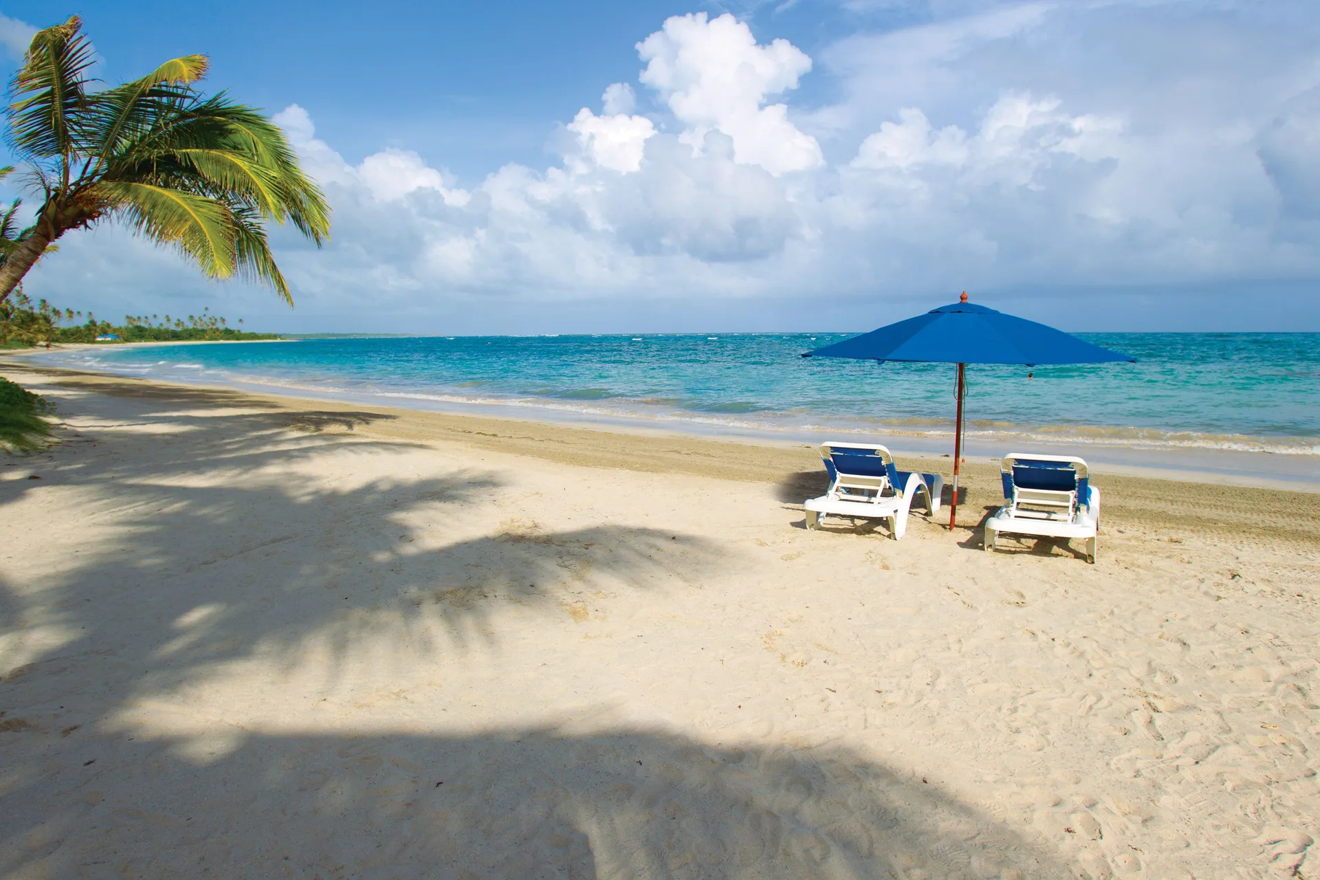 Two beach chairs and a blue umbrella on the sand at Coconut Bay Beach Resort & Spa.