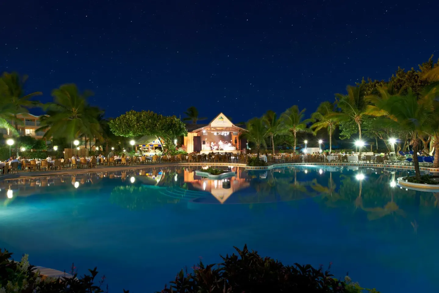 Nighttime pool scene with outdoor dining and a lit stage at Coconut Bay Beach Resort & Spa.