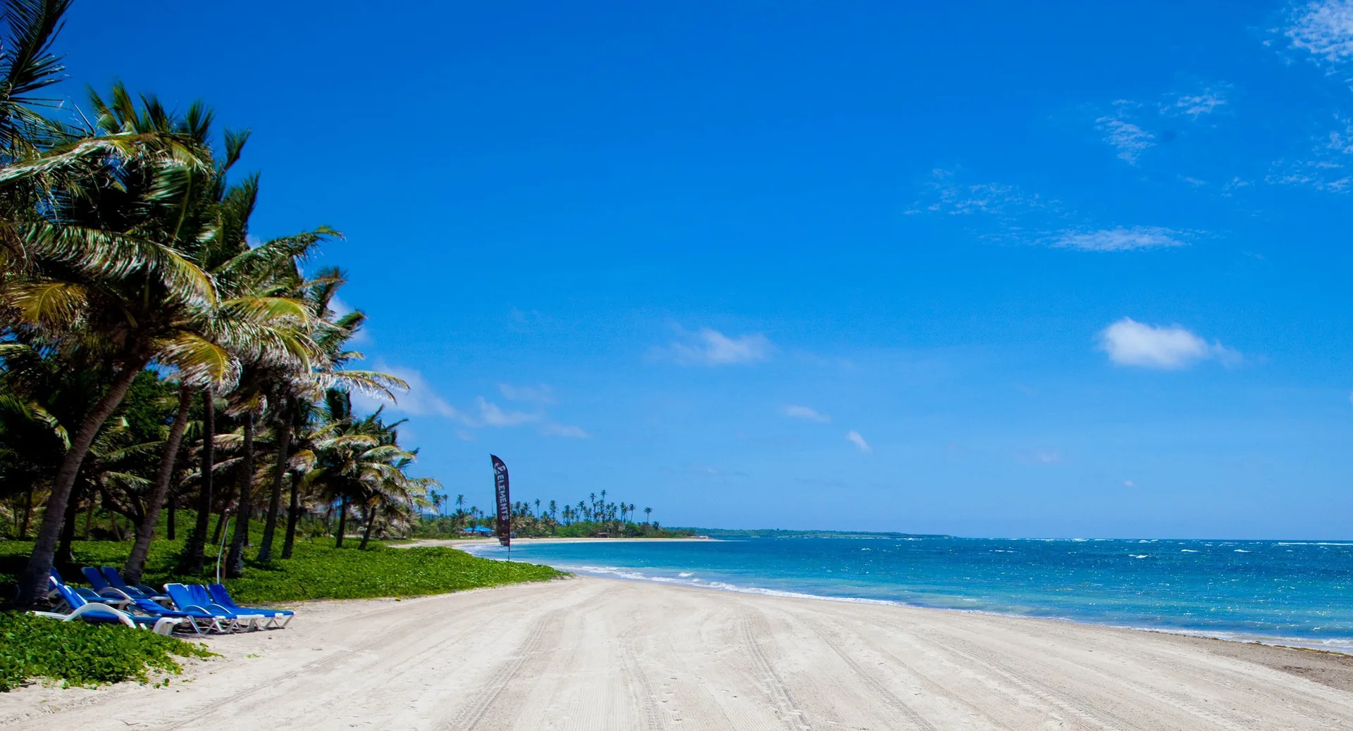 Wide sandy beach with blue loungers and palm trees at Coconut Bay Beach Resort & Spa.