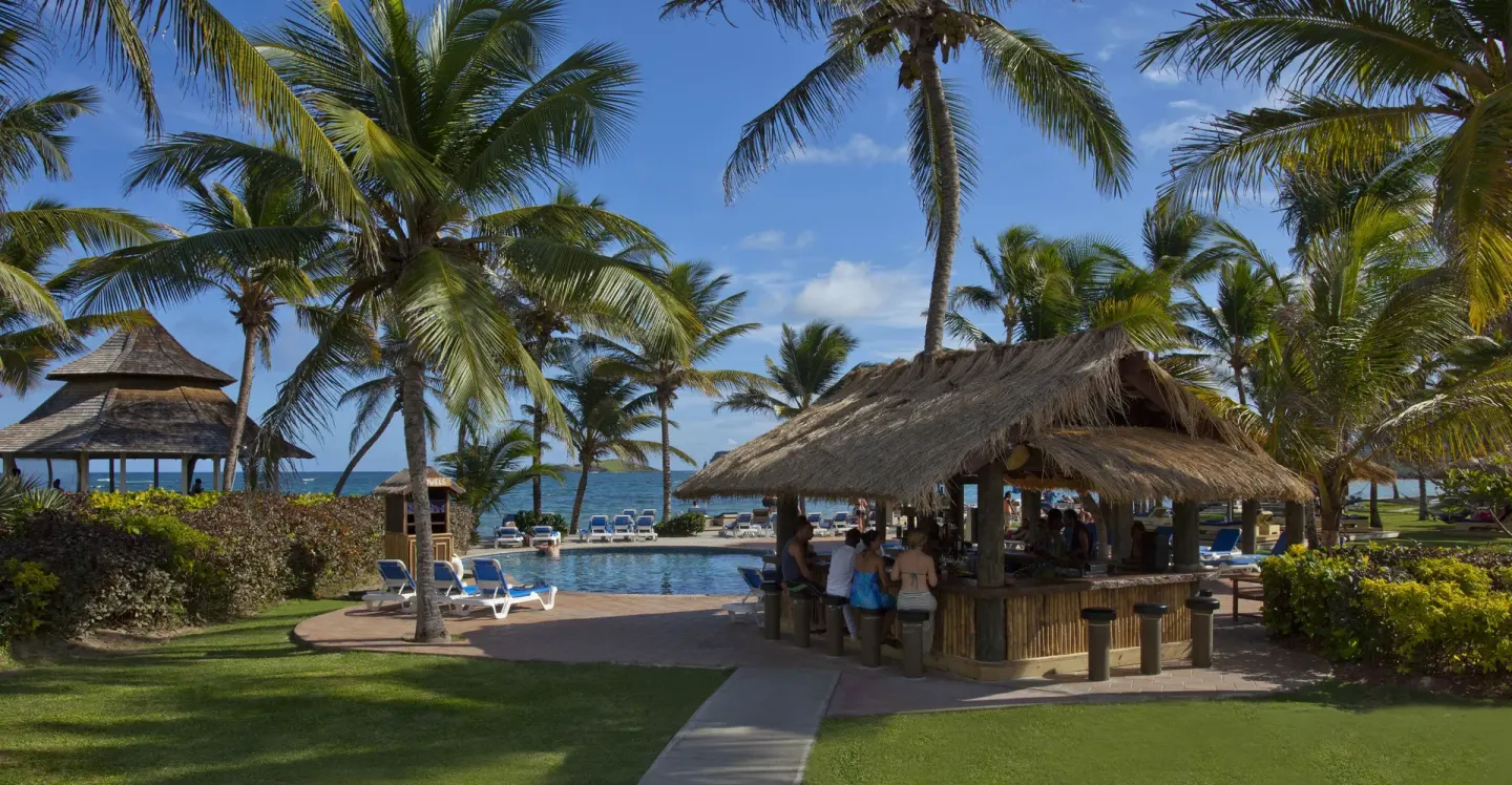 Thatched poolside bar among palms near the ocean at Coconut Bay Beach Resort & Spa.