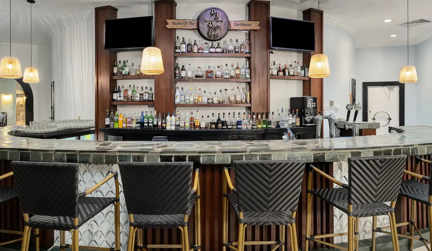 Rum bar with shelves of spirits and woven bar chairs at Coconut Bay Beach Resort & Spa.