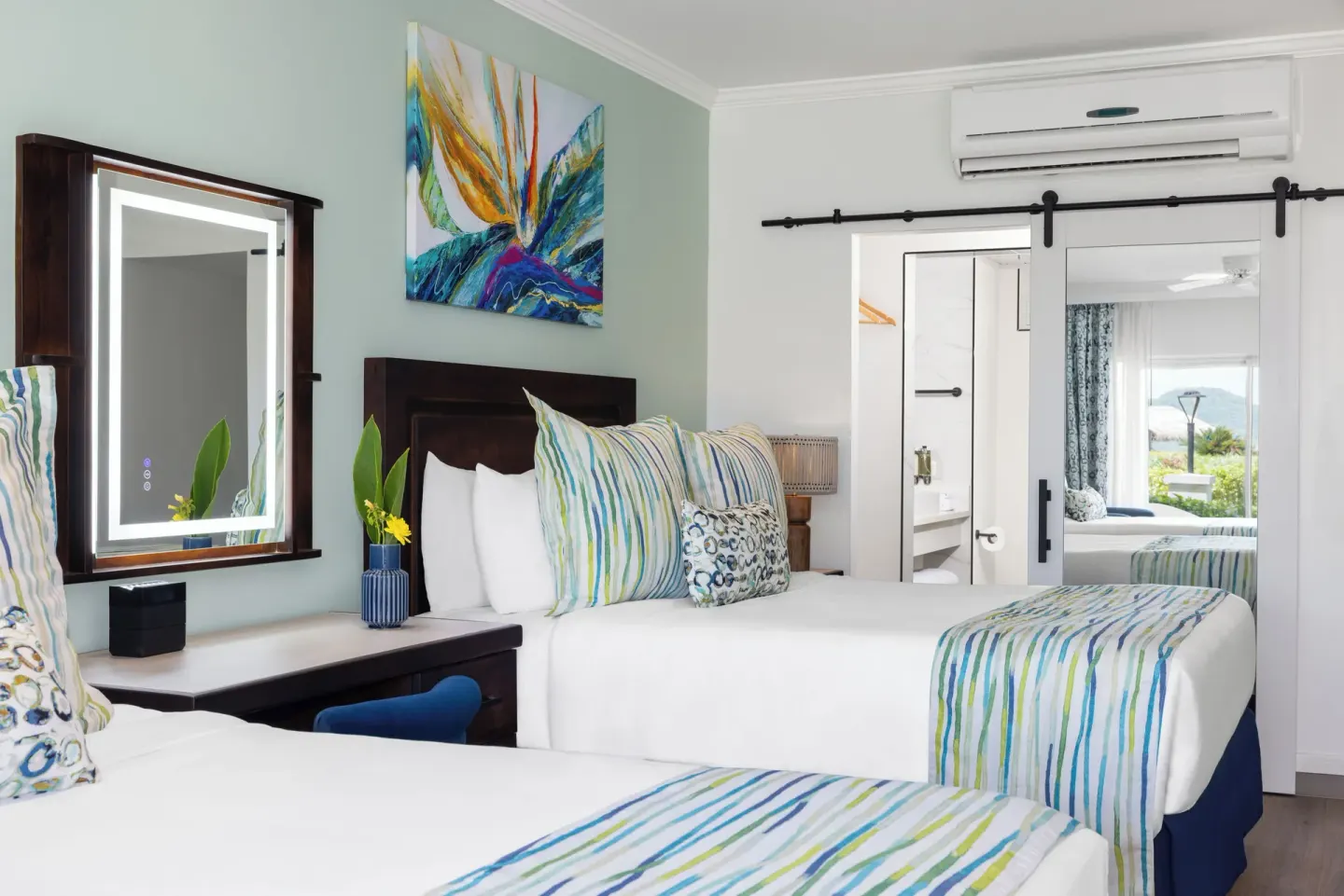 Two beds, vanity mirror, and sliding bathroom door in a Harmony JR Suite at Coconut Bay Beach Resort & Spa.