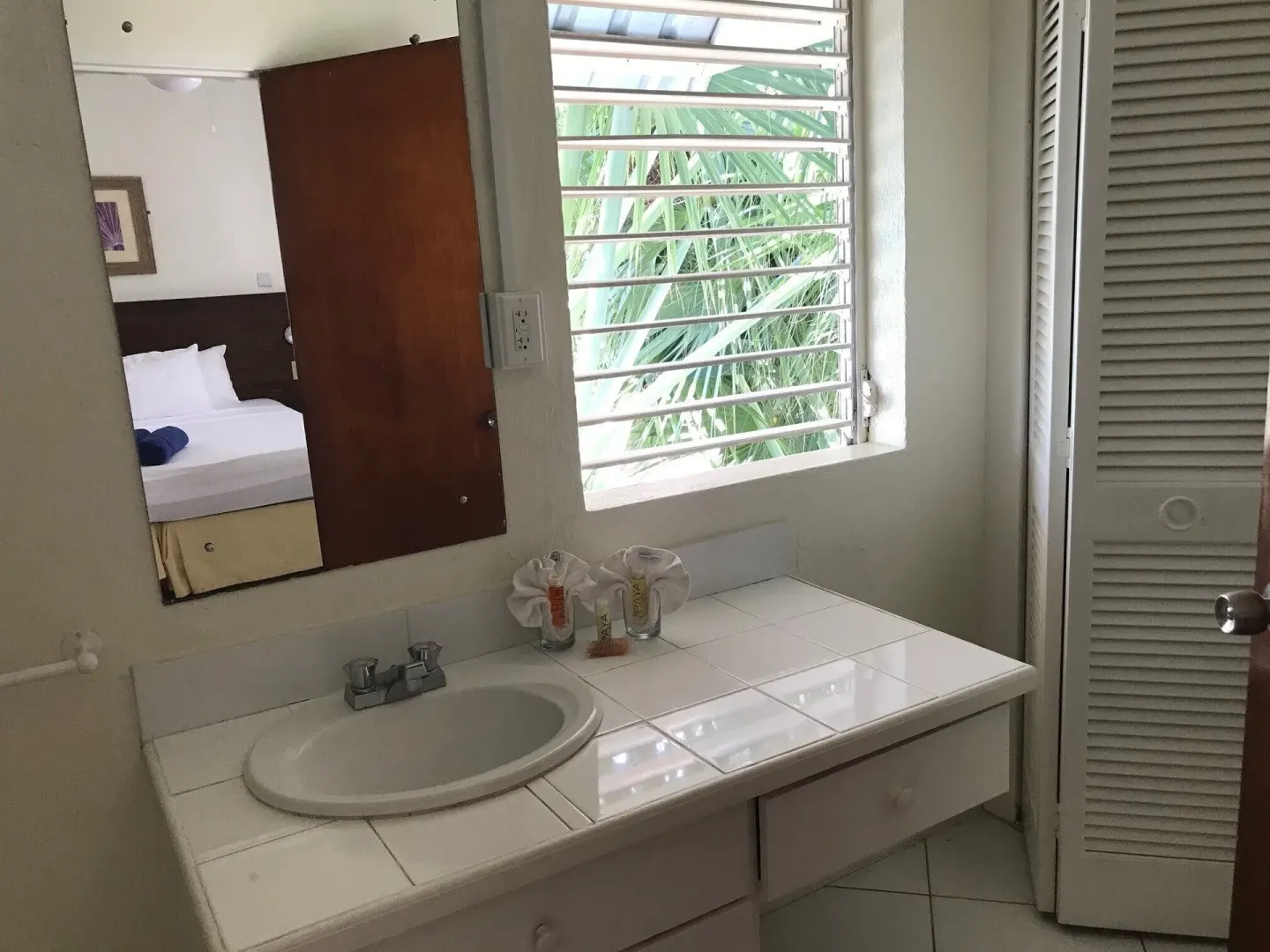 Bathroom vanity with tiled counter, mirror, and louvered window at Coconut Court Beach Hotel.