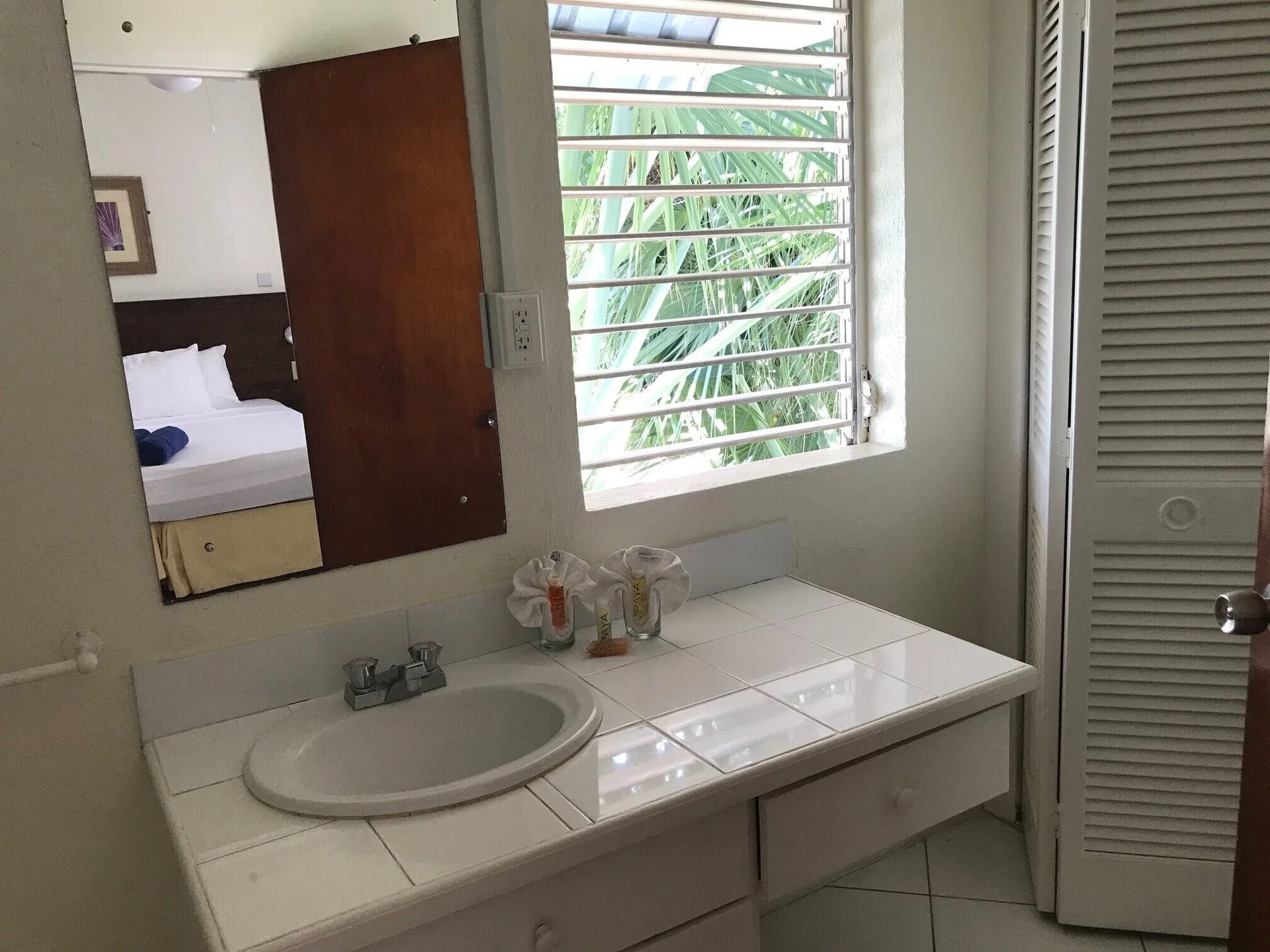 Bathroom vanity with tiled counter, mirror, and louvered window at Coconut Court Beach Hotel.