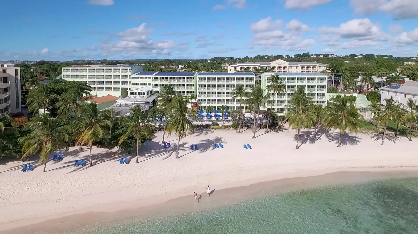 Aerial view of Coconut Court Beach Hotel beside a sandy beach and turquoise water.