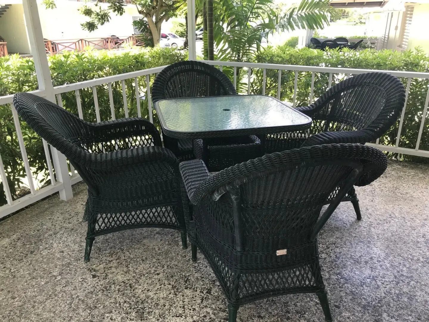 Covered patio with black wicker chairs and a glass-top table at Coconut Court Beach Hotel.