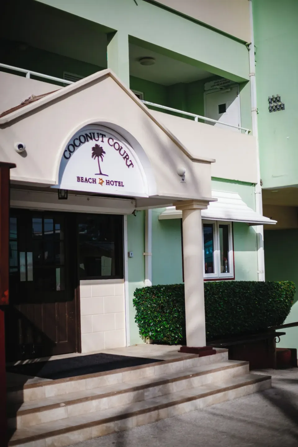 Entrance sign and steps at Coconut Court Beach Hotel with balconies above.
