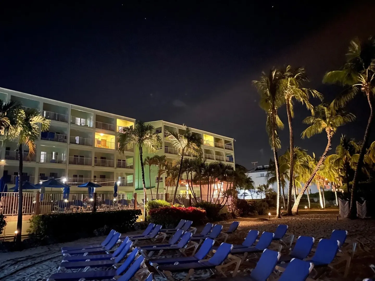 Night view of resort buildings, palms, and beach loungers at Coconut Court Beach Hotel.