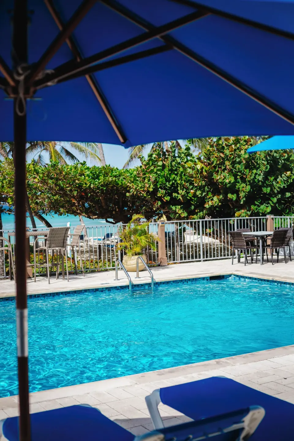 Pool water and blue umbrella shade beside the beach at Coconut Court Beach Hotel.
