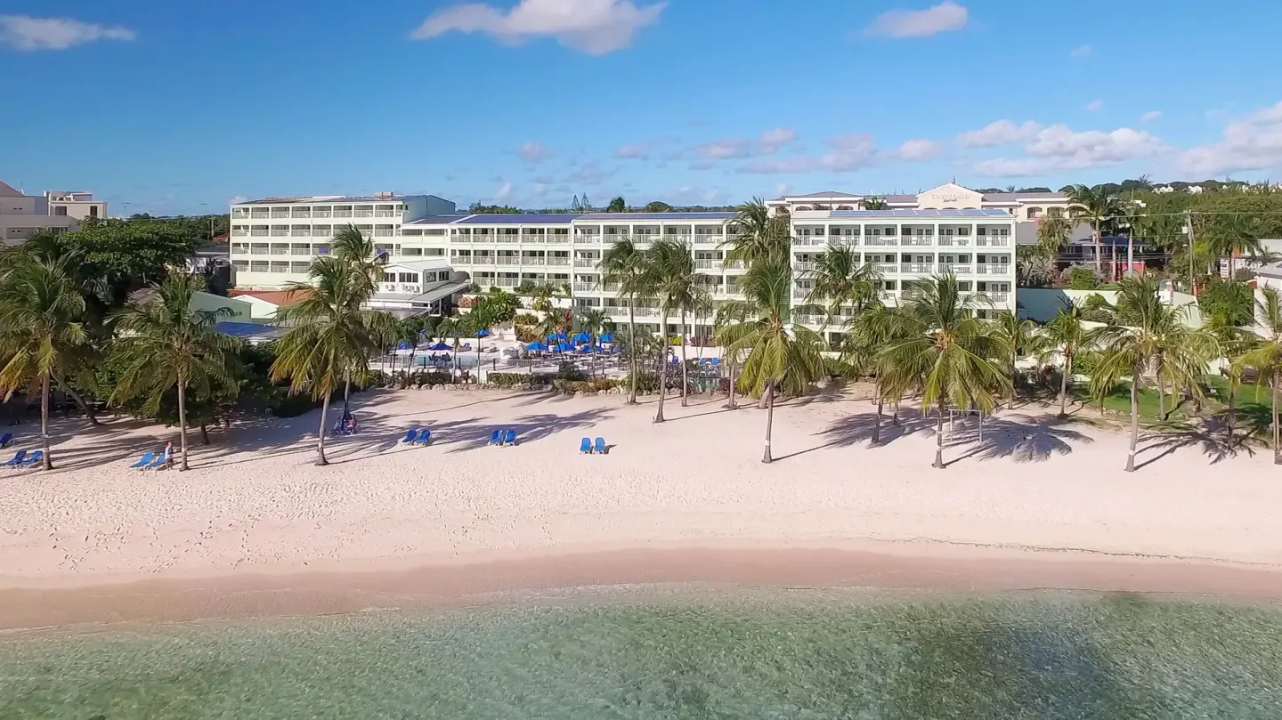 Wide beachfront view of Coconut Court Beach Hotel with palms, loungers, and clear water.
