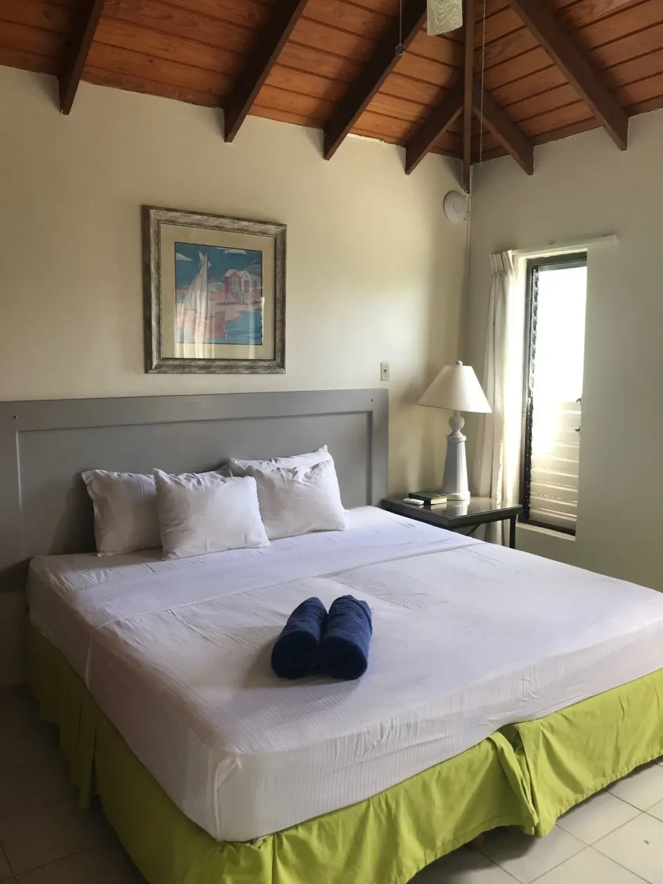 King bed with blue towels and a wood ceiling in the apartment at Coconut Court Beach Hotel.