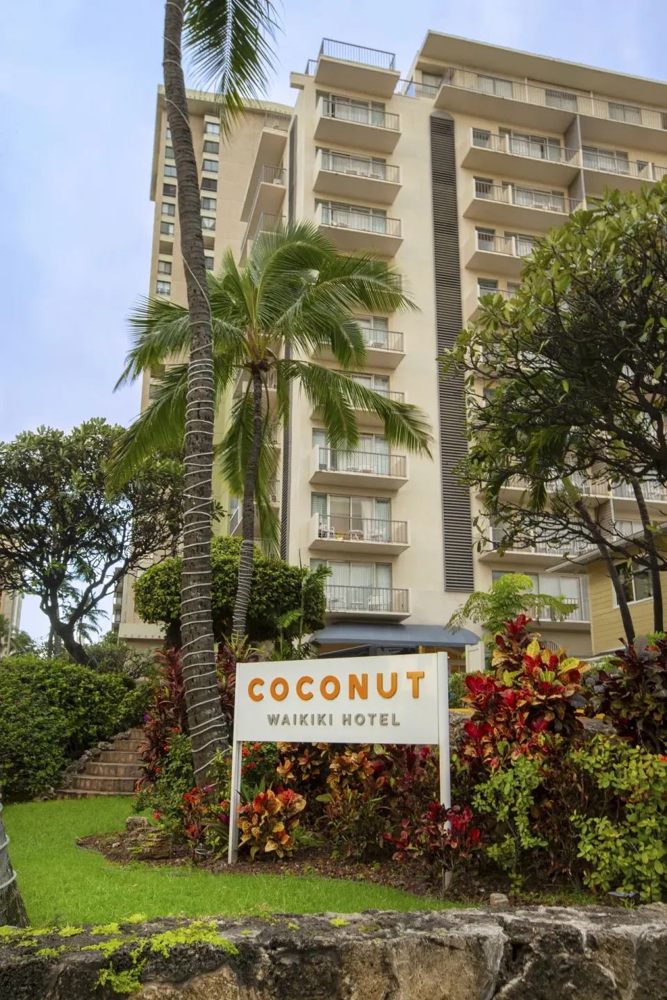 Hotel exterior with balconies, palm trees, and entrance sign at Coconut Waikiki Hotel.