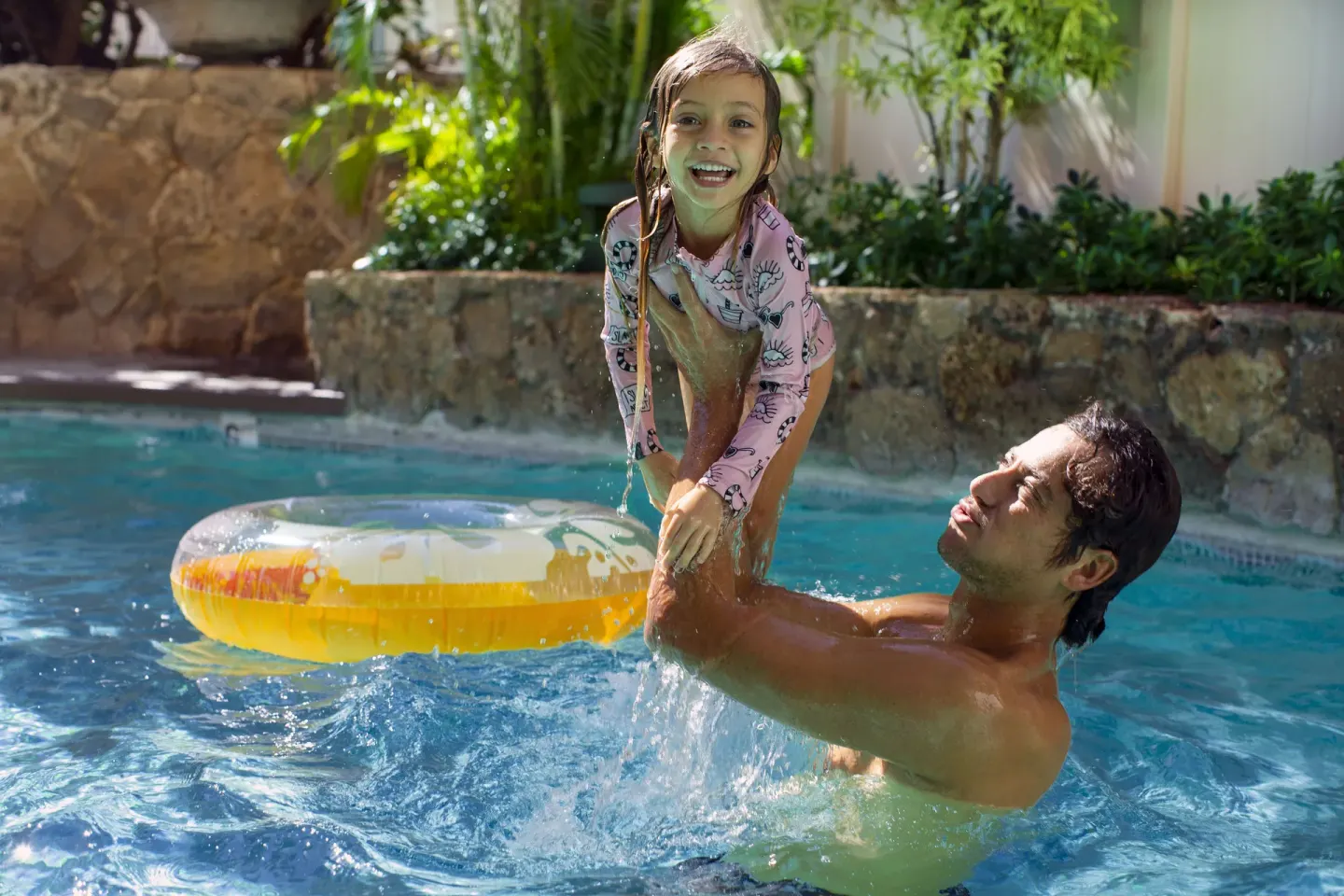 Adult lifting a smiling child in the pool at Coconut Waikiki Hotel.