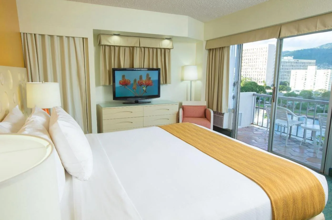 Guest room with a king bed, TV, dresser, and balcony at Coconut Waikiki Hotel.