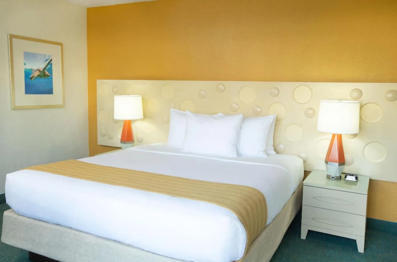 Guest room with one king bed and orange accent wall at Coconut Waikiki Hotel.