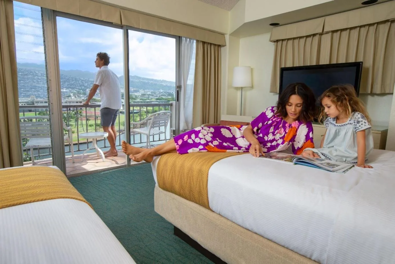 Guest room with two beds, balcony, and people relaxing at Coconut Waikiki Hotel.
