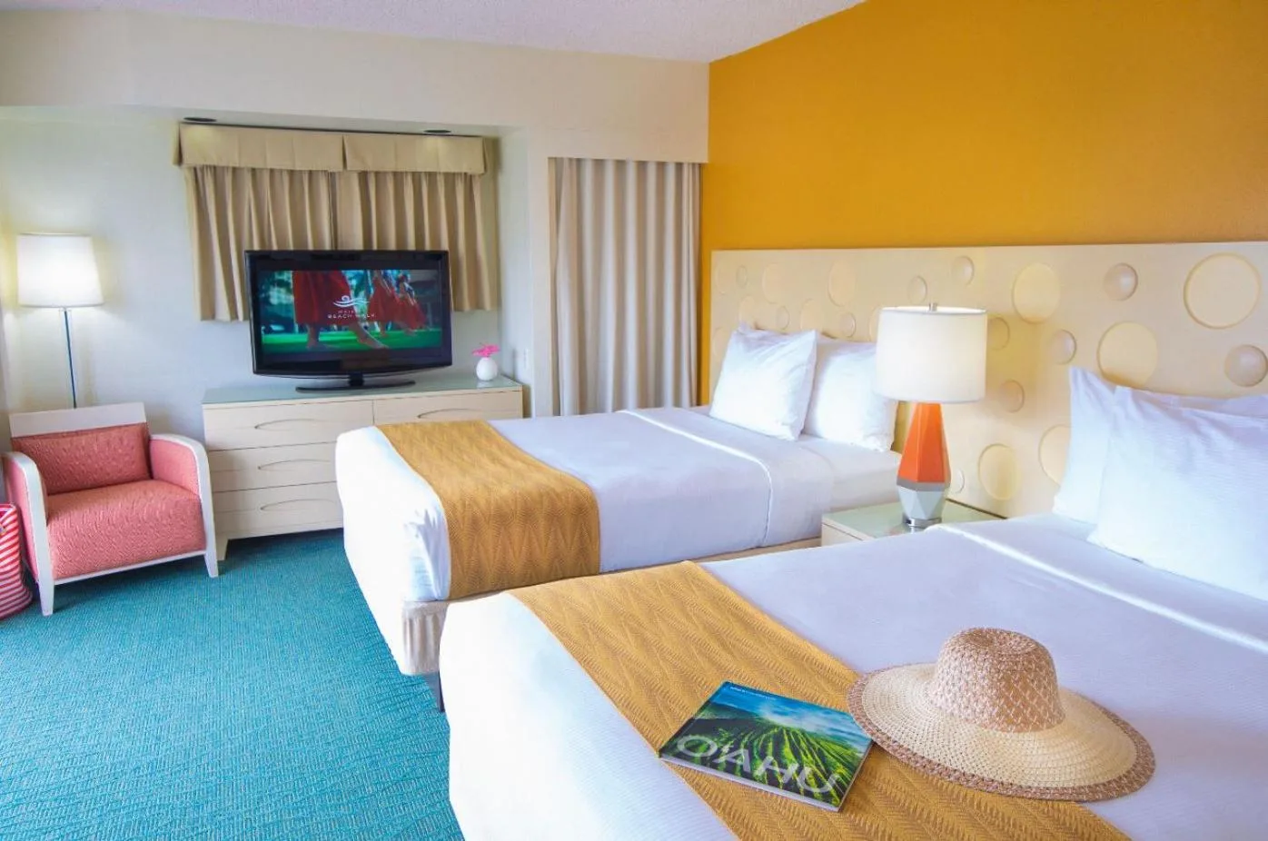 Guest room with two beds, TV, and orange accent wall at Coconut Waikiki Hotel.