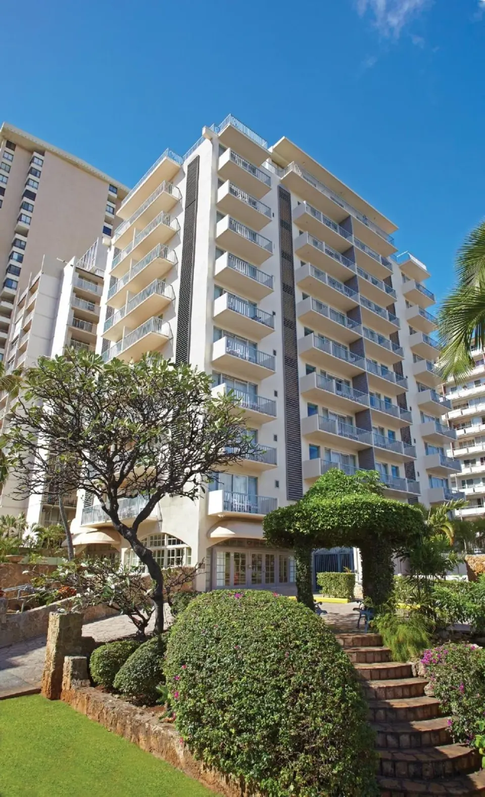 Hotel exterior with balconies, landscaping, and blue sky at Coconut Waikiki Hotel.