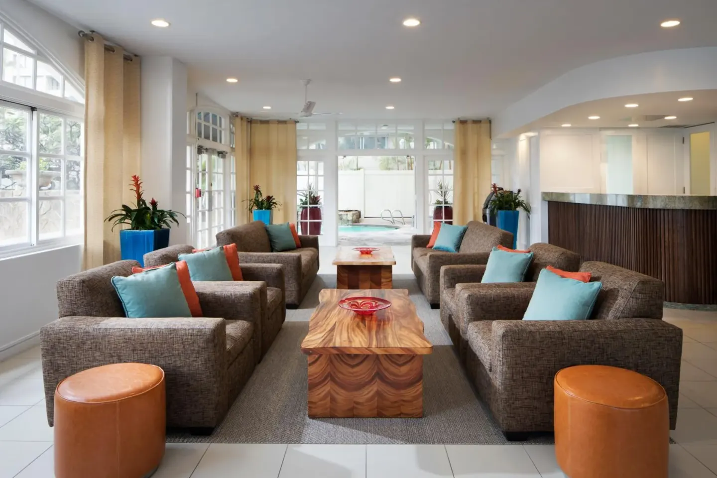 Lobby seating area with sofas, bright pillows, and pool beyond at Coconut Waikiki Hotel.