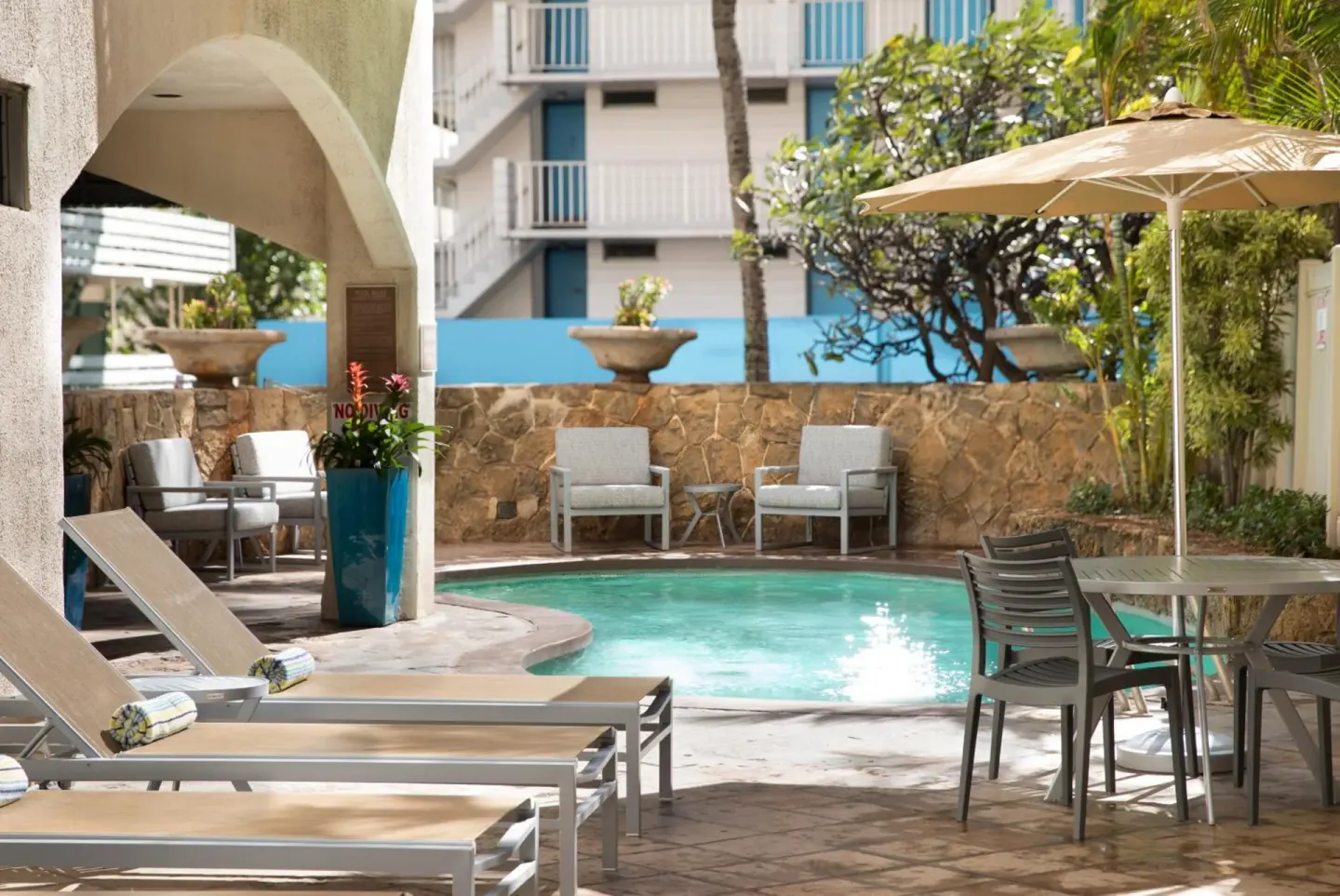 Pool courtyard with lounge chairs and patio table at Coconut Waikiki Hotel.
