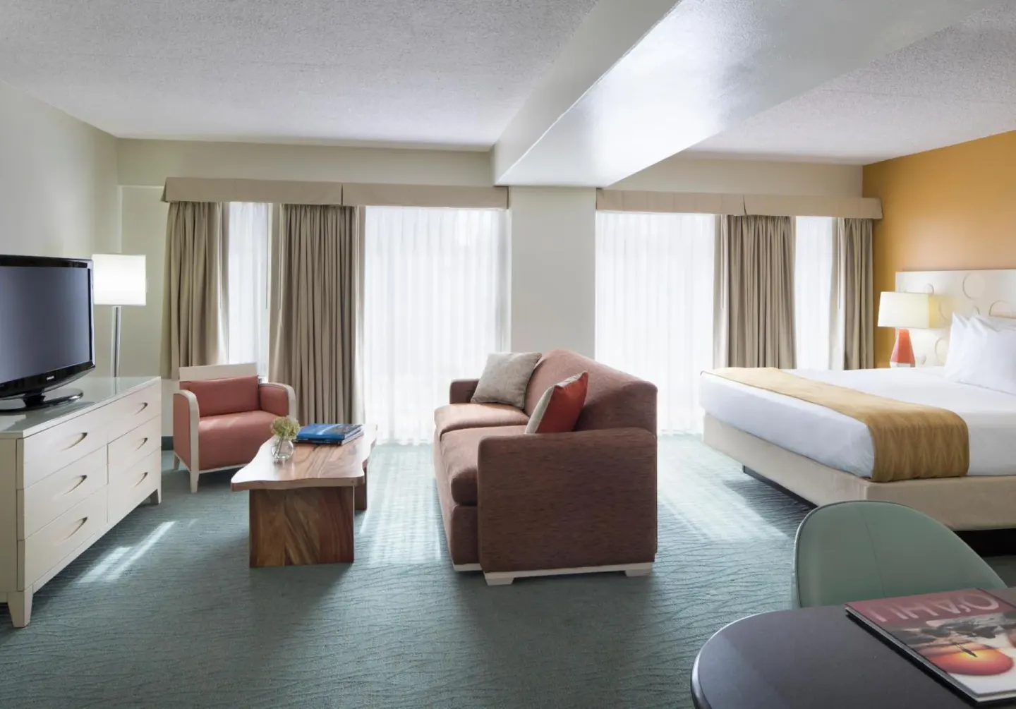 Spacious suite with king bed, sofa, TV, and sitting area at Coconut Waikiki Hotel.