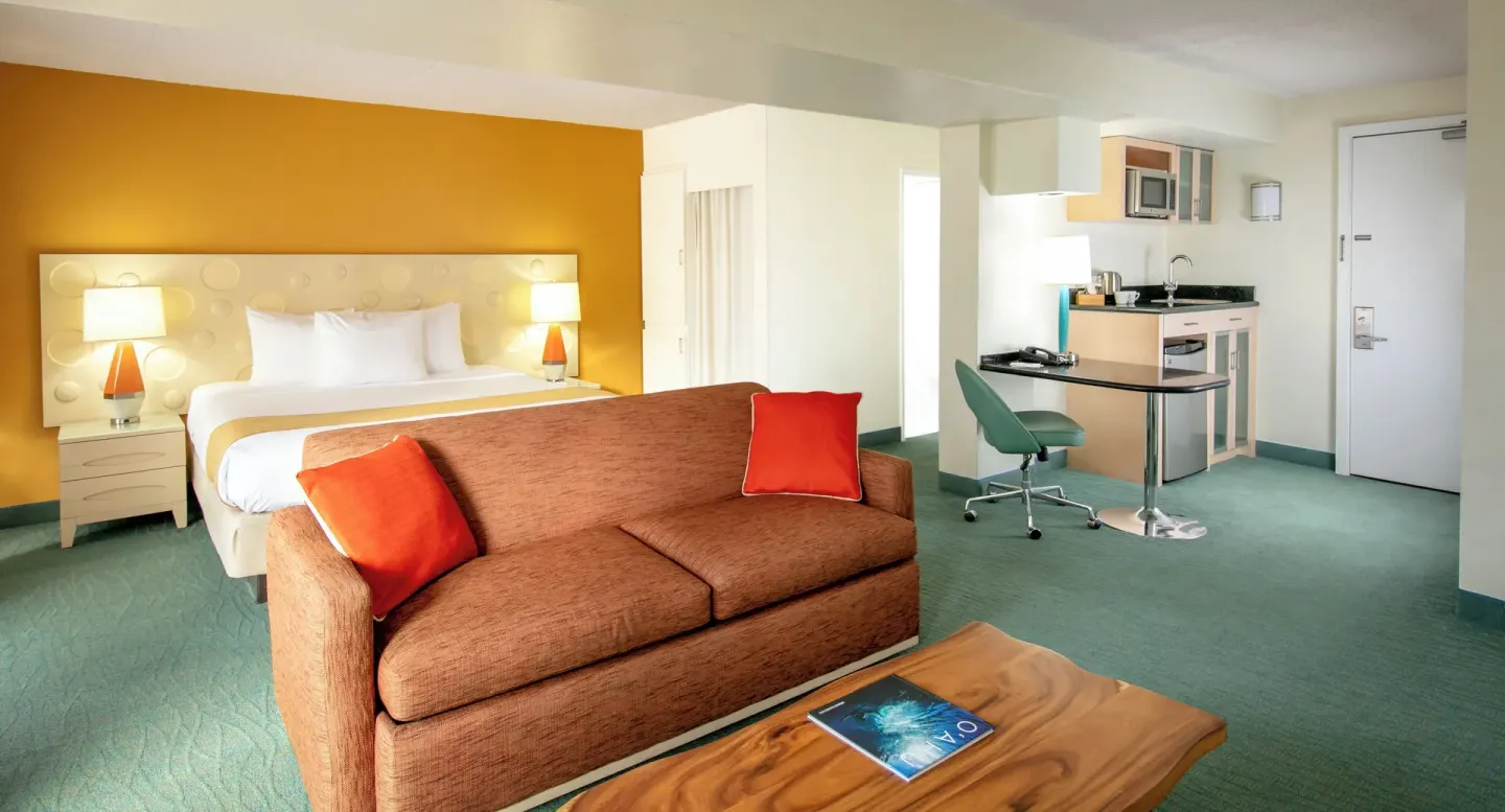Executive Suite with king bed, sofa, coffee table, kitchenette, and entry door at Coconut Waikiki Hotel.