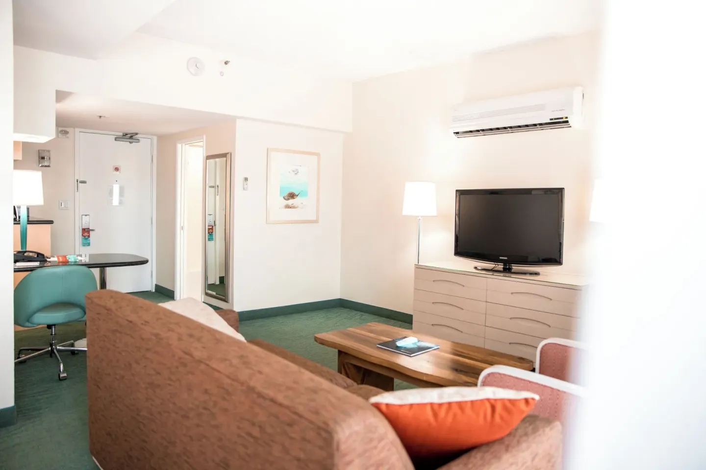 Executive Suite seating area with TV, coffee table, desk, and entry door at Coconut Waikiki Hotel.