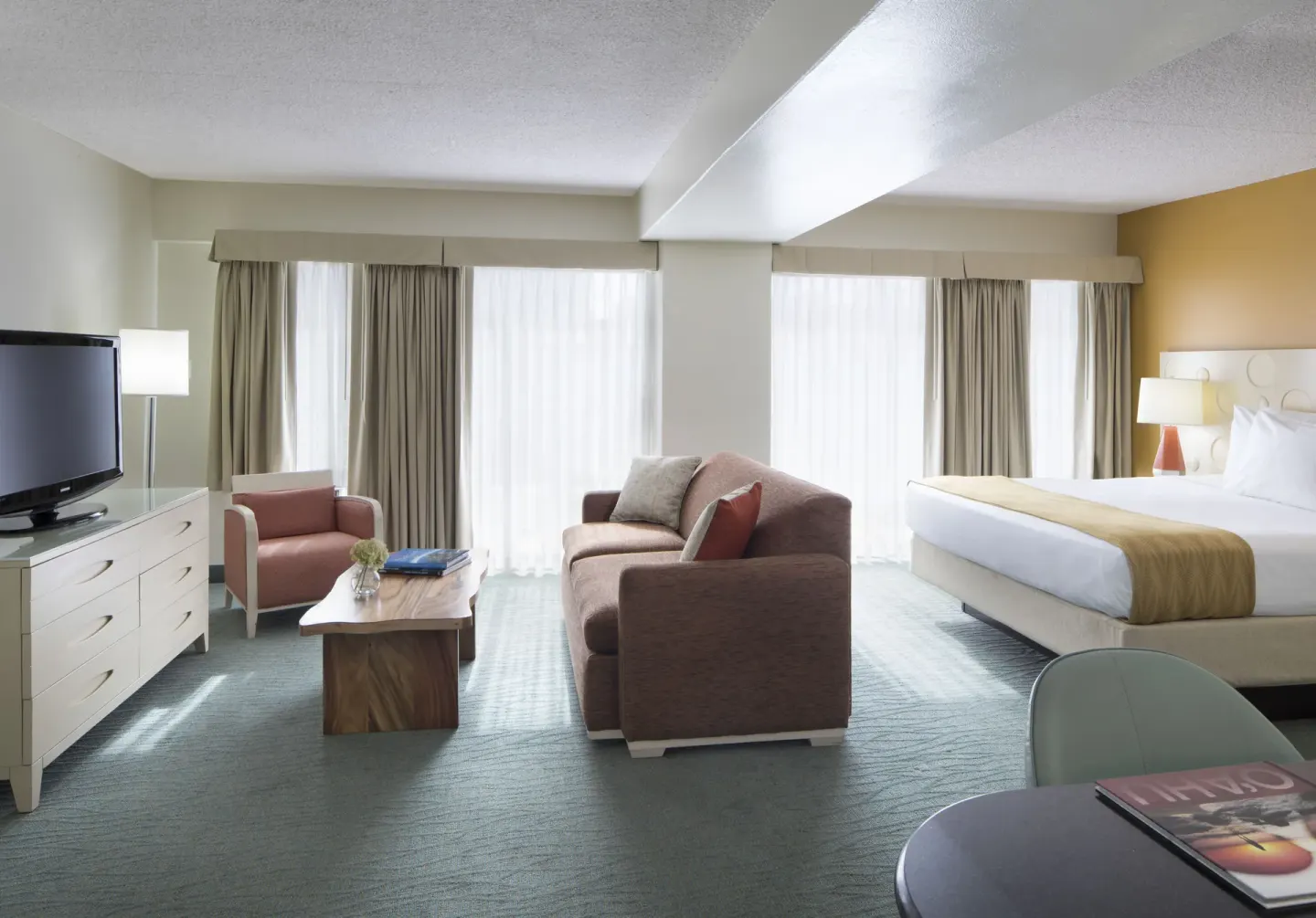 Executive Suite with king bed, sofa seating, TV, and bright windows at Coconut Waikiki Hotel.