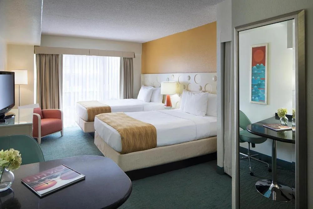 Mountain View Room at Coconut Waikiki Hotel with two beds, a sitting chair, TV, and small table area.
