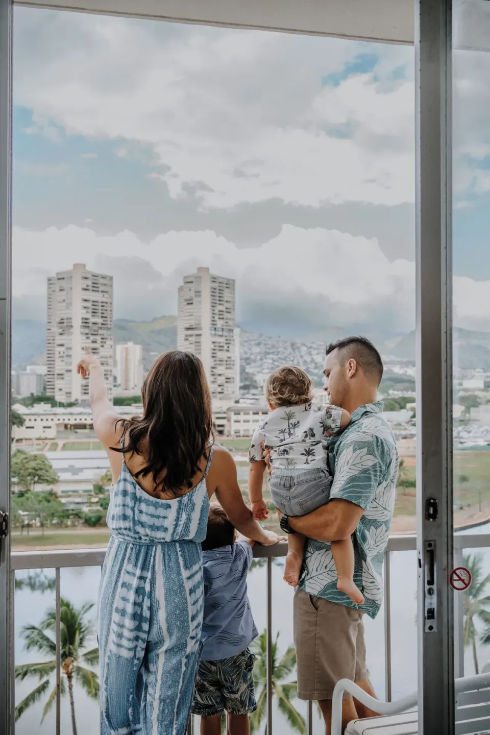 Standard Room City View balcony with family overlooking Honolulu at Coconut Waikiki Hotel.