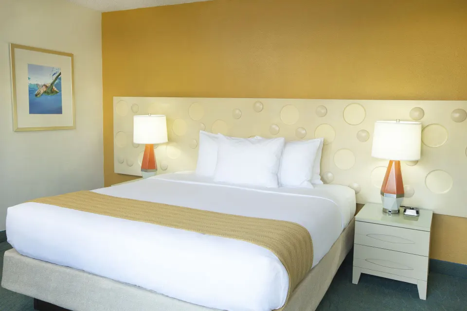 Standard Room City View king bed with lamps and gold accent wall at Coconut Waikiki Hotel.