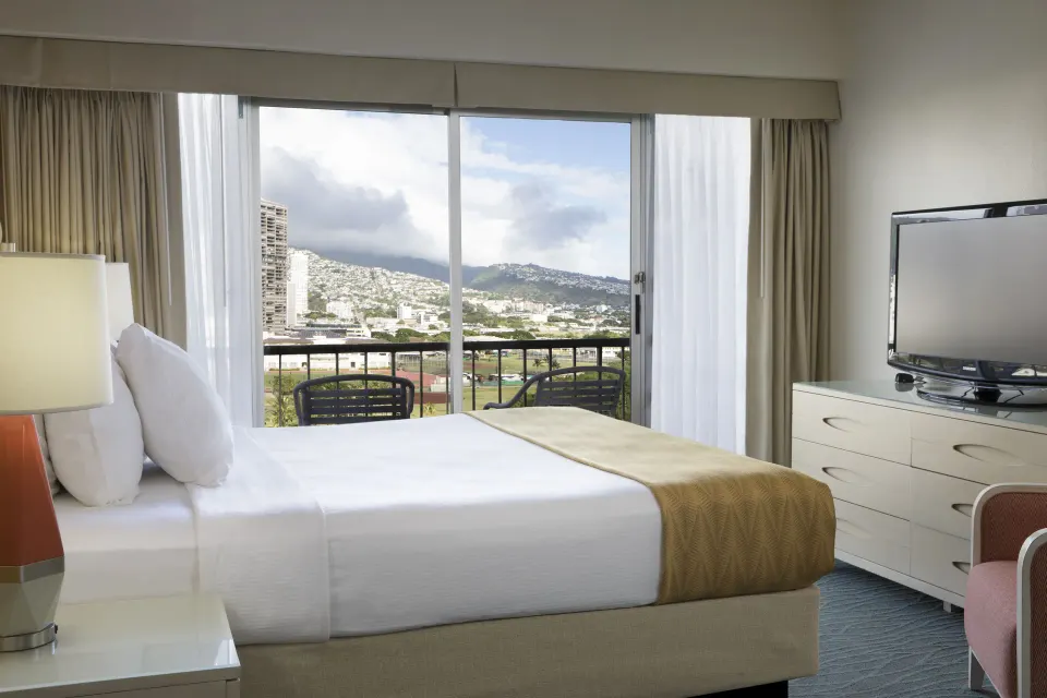 Standard Room Mountain View king bed with balcony and dresser at Coconut Waikiki Hotel.