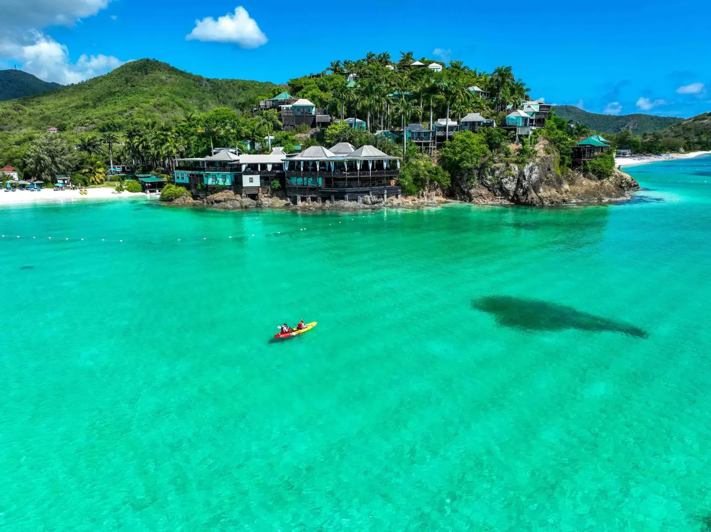 Aerial view of COCOS Hotel on a rocky point above turquoise water with a small kayak in the bay.
