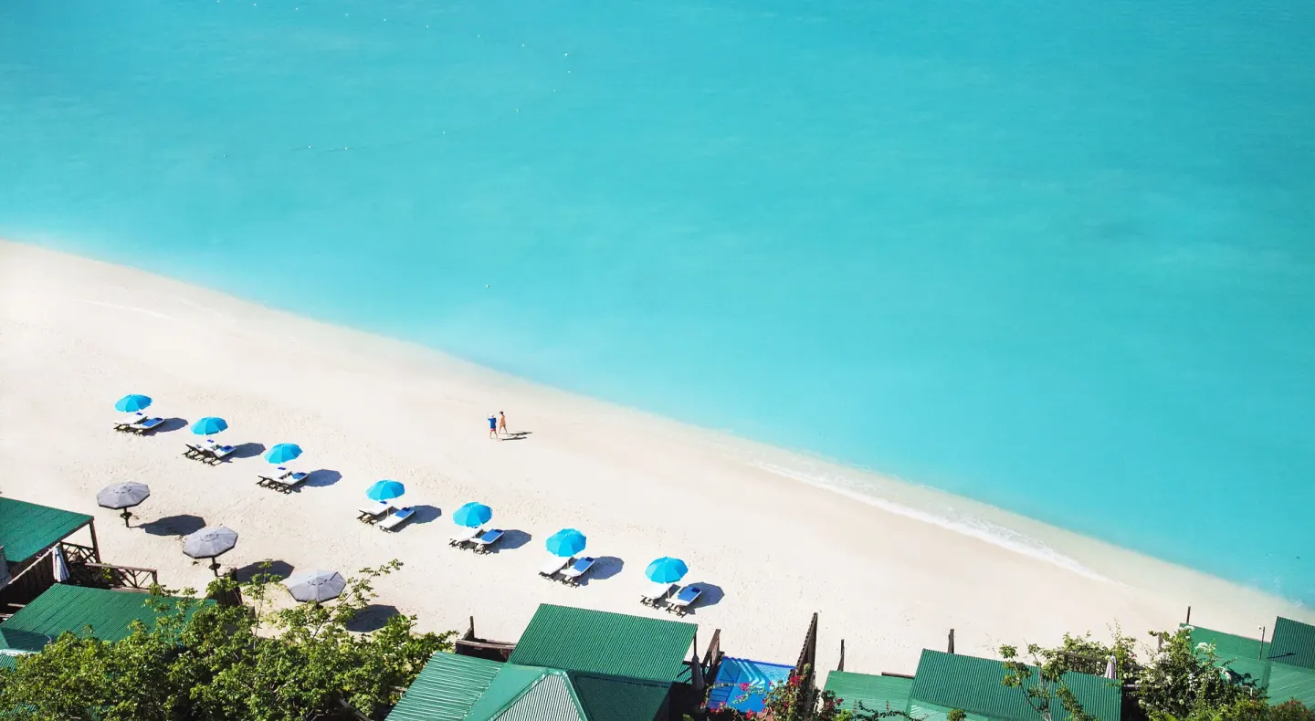 Aerial view of beach umbrellas and turquoise water at COCOS Hotel.