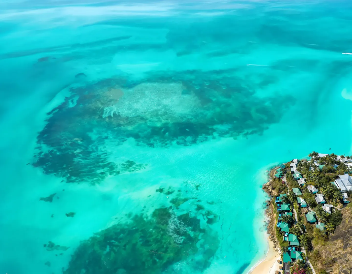 High aerial view of COCOS Hotel beside shallow turquoise water and dark reef patches.