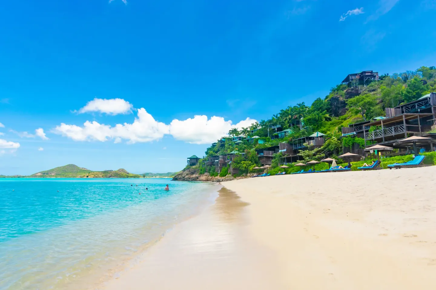Sandy beach and hillside cottages beside turquoise water at COCOS Hotel.