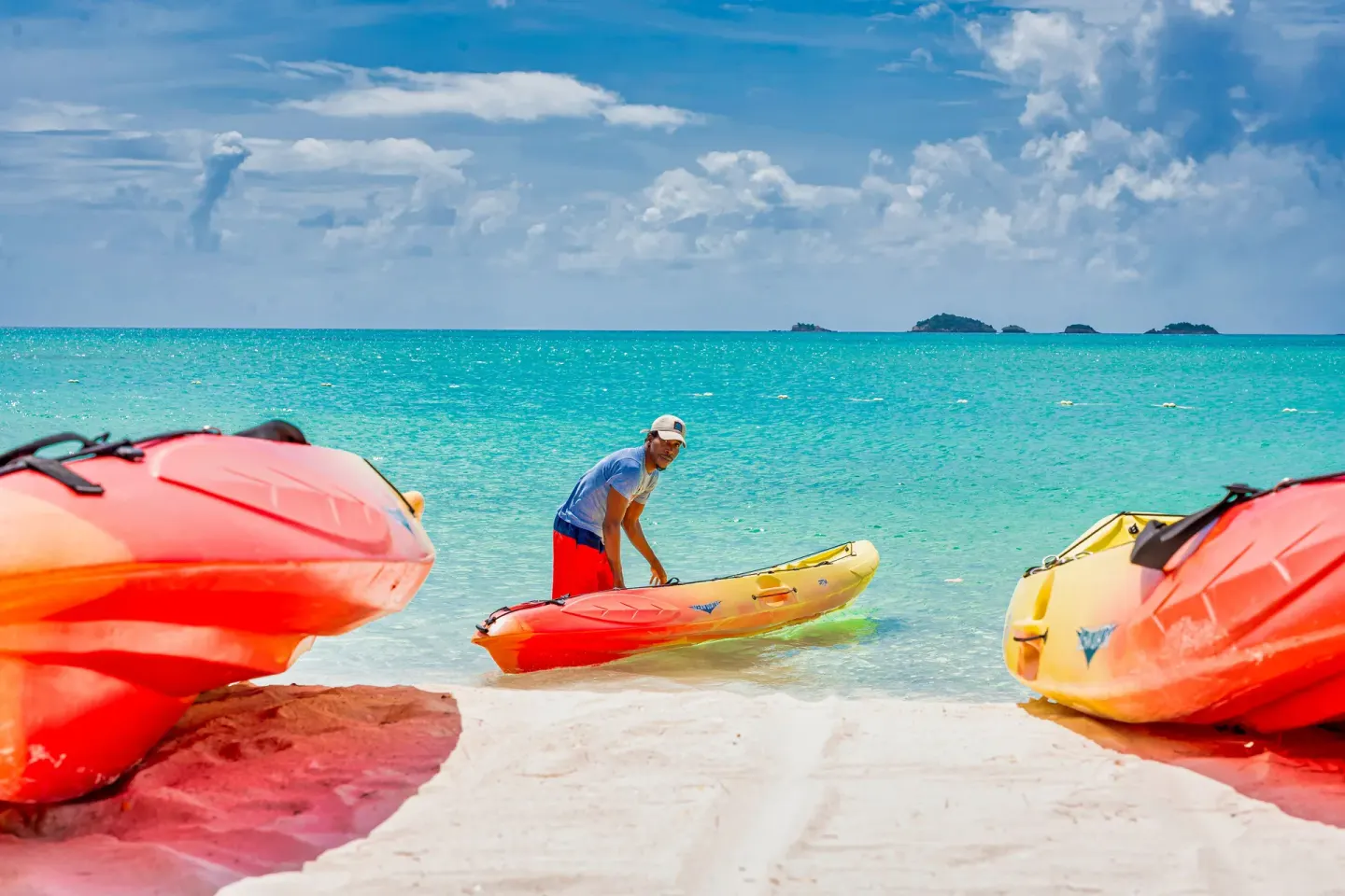 Colorful kayaks rest on the sand by turquoise water at COCOS Hotel.