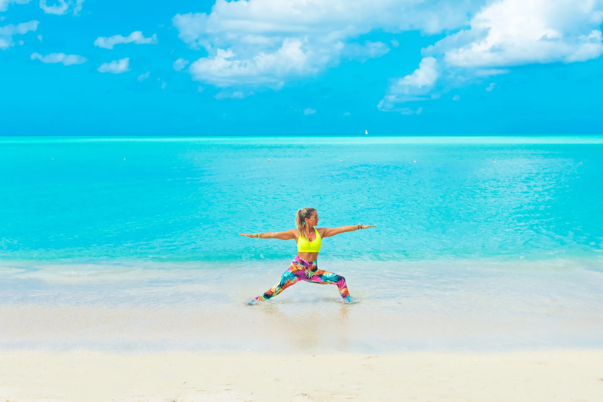 Guest doing yoga on the sandy beach beside turquoise water at COCOS Hotel.