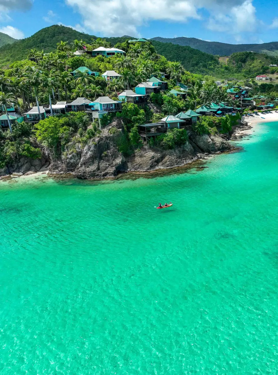 Cliffside cottages and a small kayak on turquoise water at COCOS Hotel.
