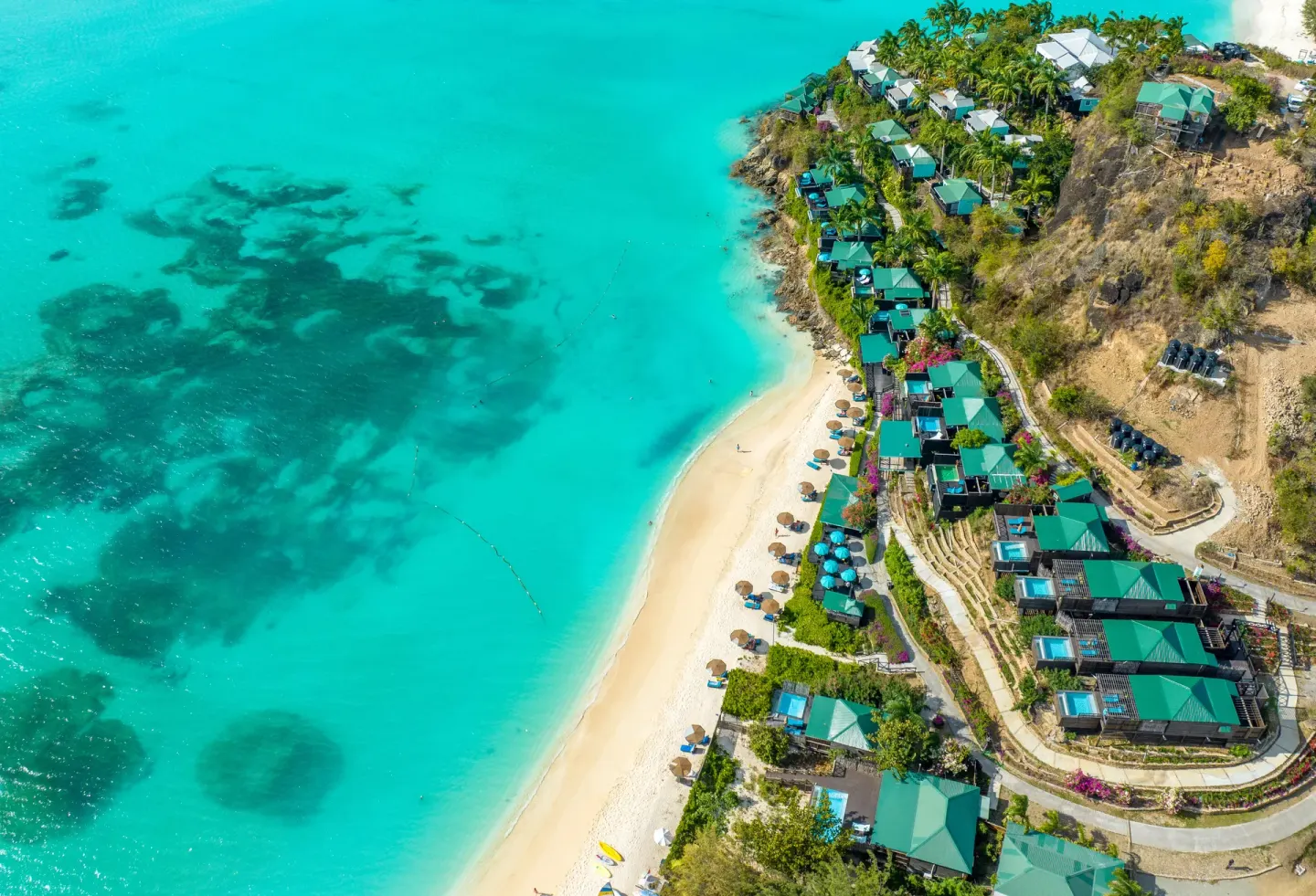 Drone view of beach, hillside cottages, and reef-colored water at COCOS Hotel.