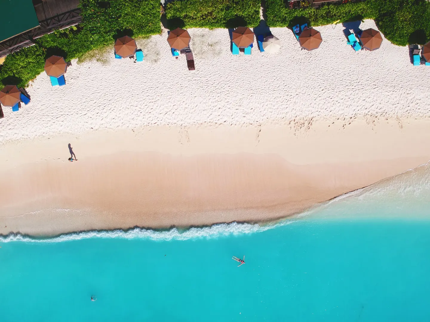 Overhead view of beach loungers, umbrellas and turquoise sea at COCOS Hotel.