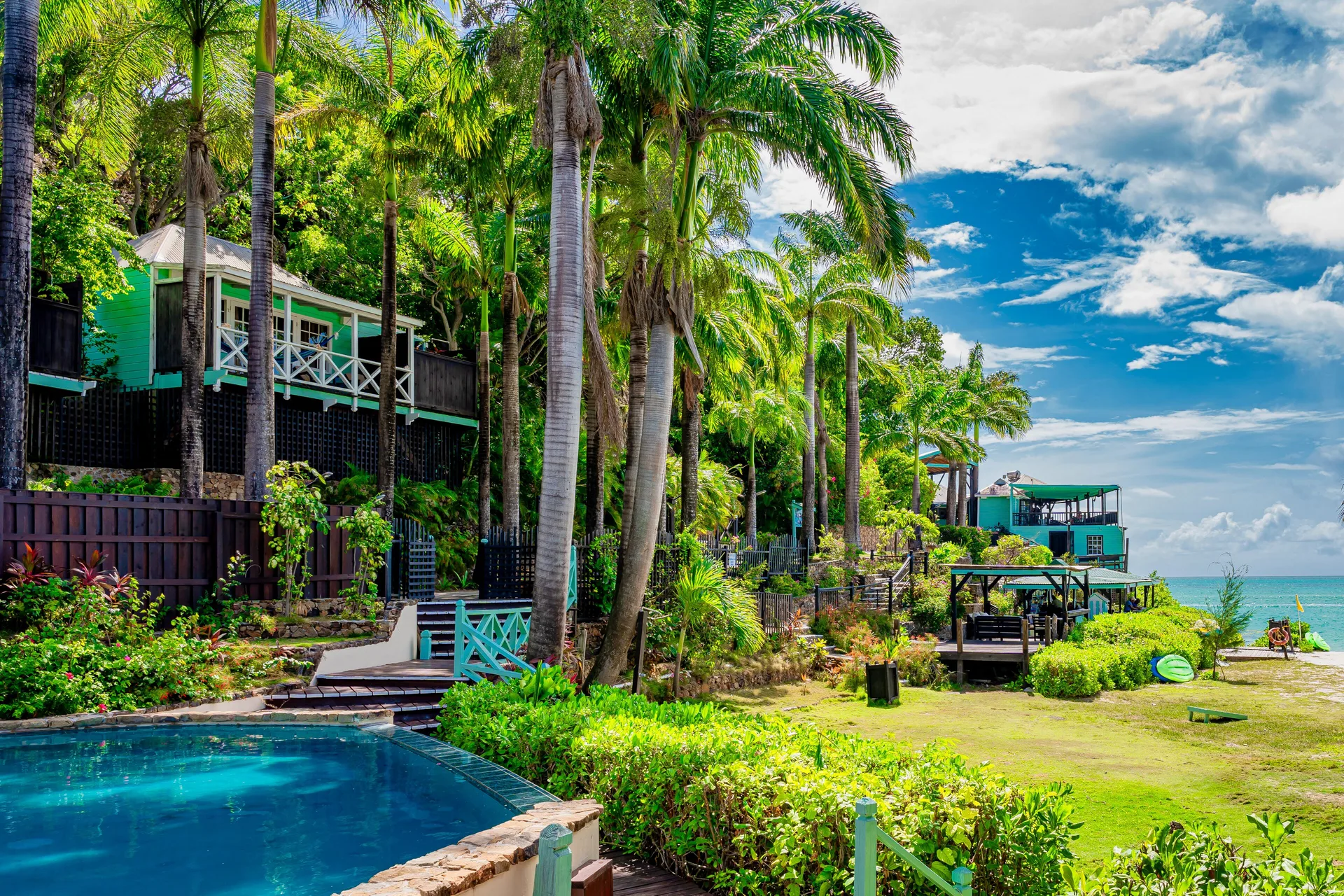 Pool, garden lawn, palms, and hillside cottages overlooking the sea at COCOS Hotel.