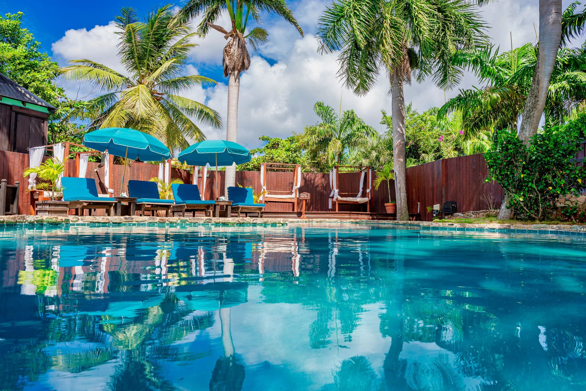 Low view across the pool at COCOS Hotel toward blue loungers, umbrellas, palms, and cabanas.