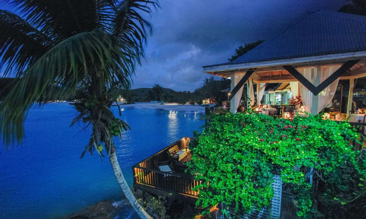 Illuminated seaside building and deck at night at COCOS Hotel.