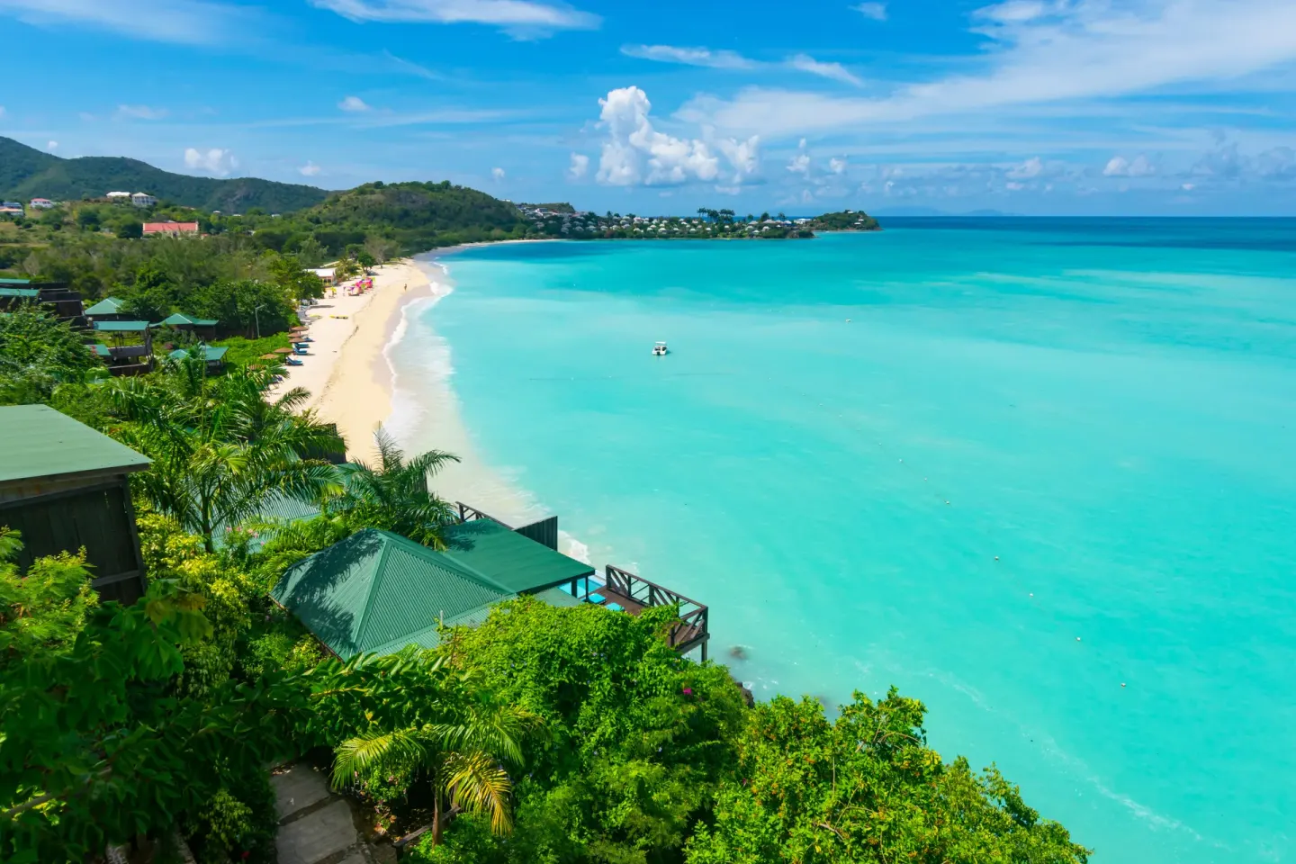 Wide turquoise bay with beach and hillside cottages at COCOS Hotel.