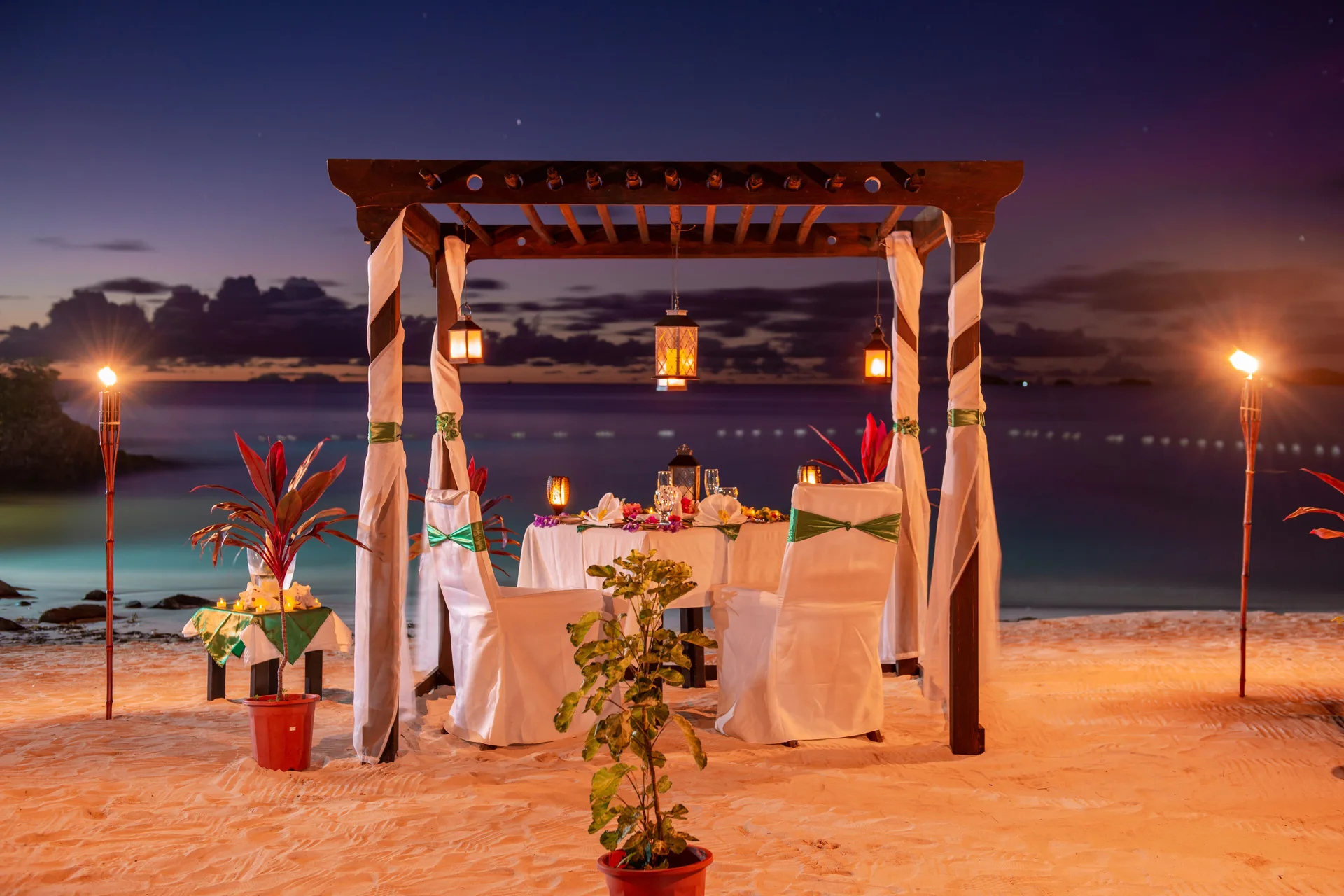 Private beach dinner setup under a lit pergola at COCOS Hotel.