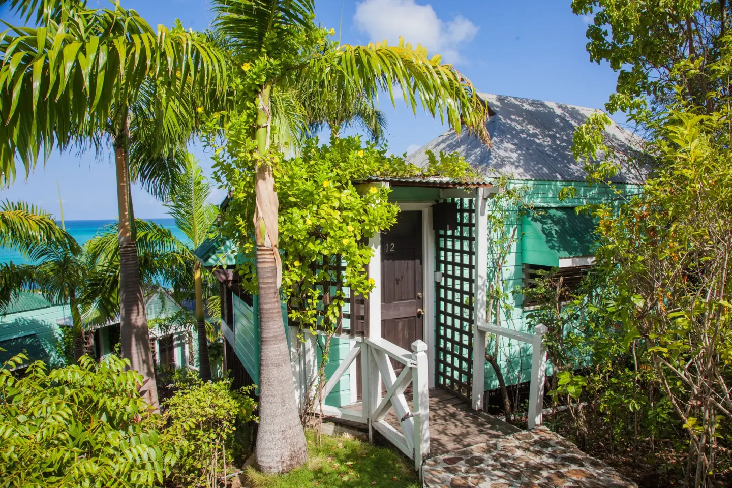 Premium View Cottage exterior among palms with sea glimpses at COCOS Hotel.