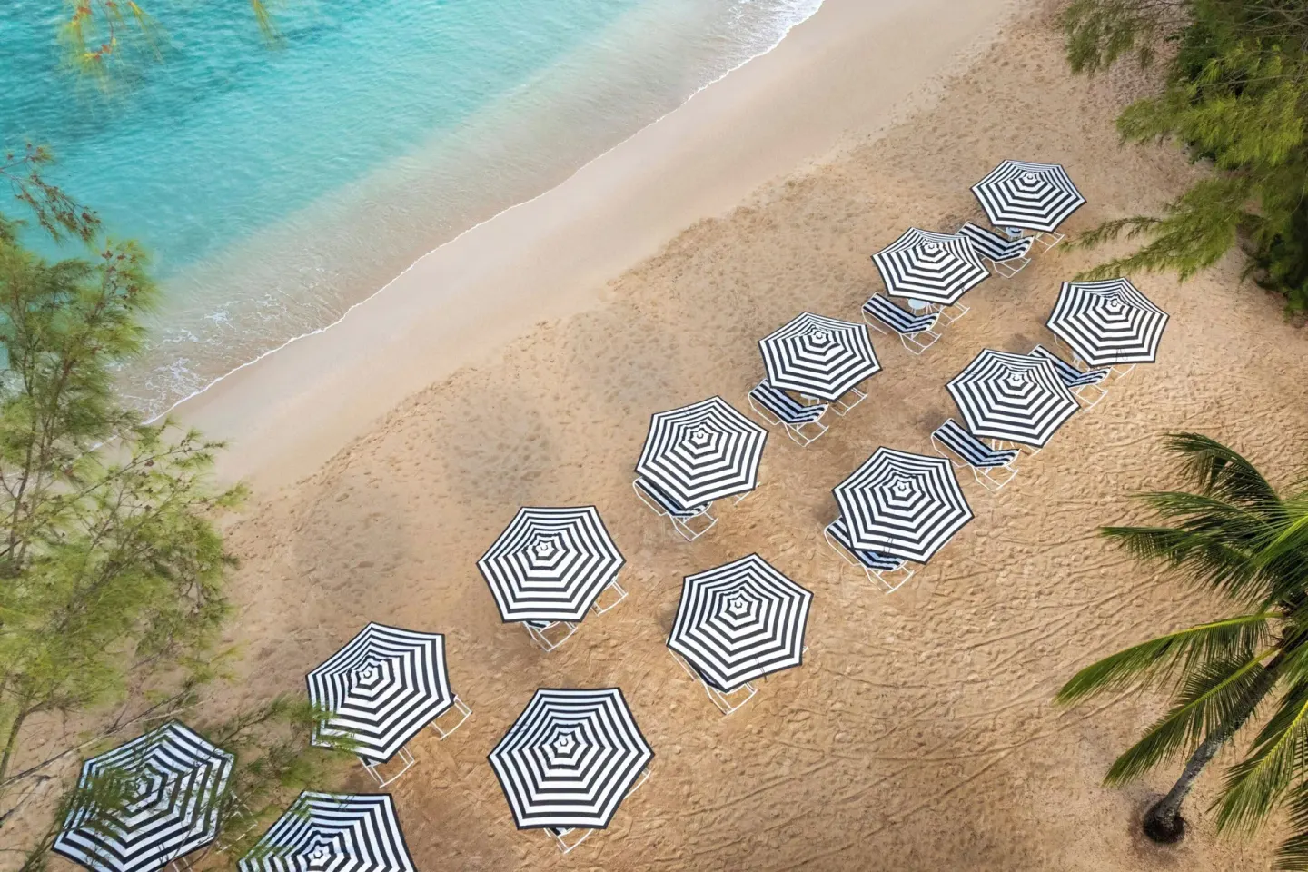 Aerial view of striped beach umbrellas on the sand at Colony Club, Barbados.