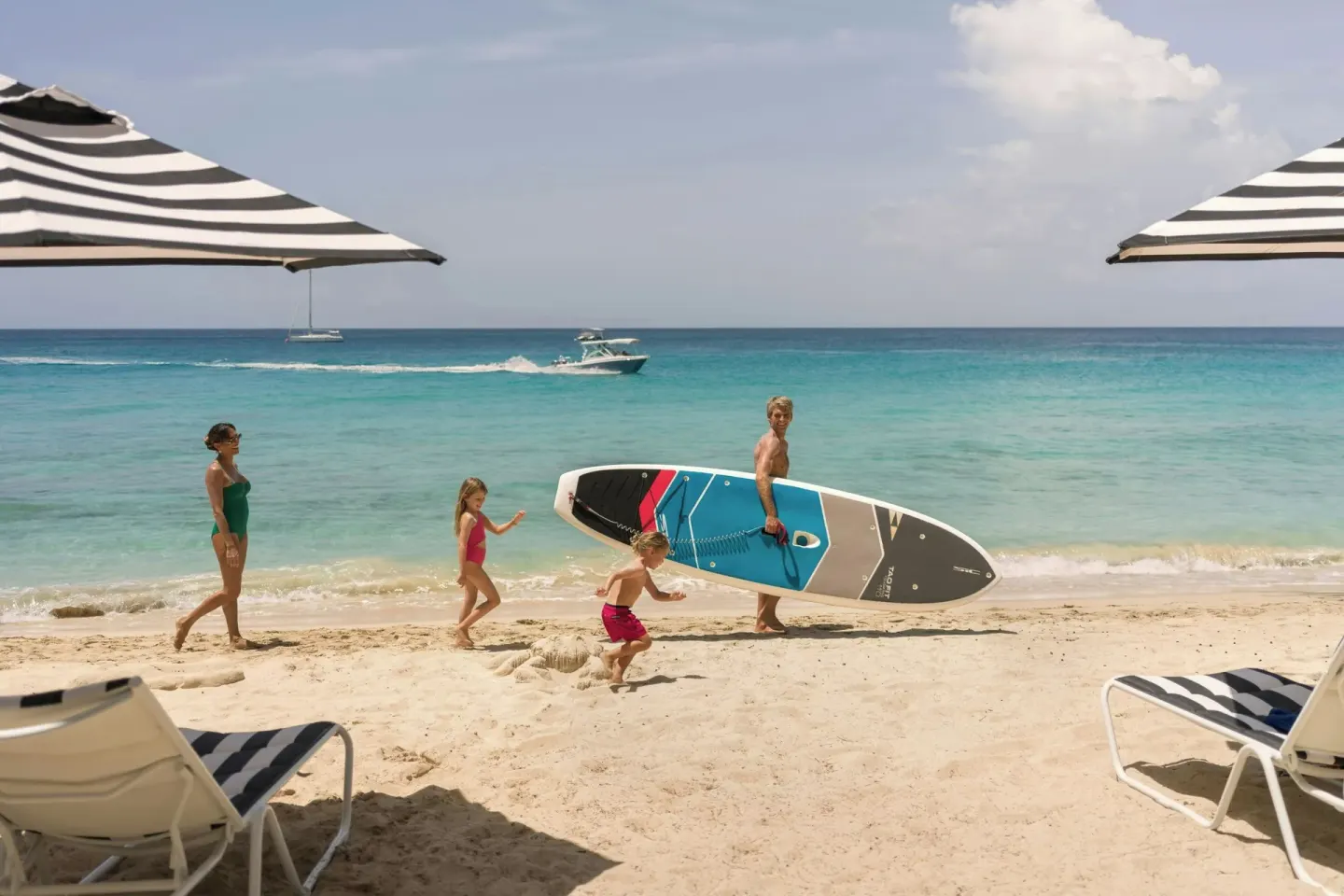 Family walking on the beach with a paddleboard at Colony Club, Barbados.